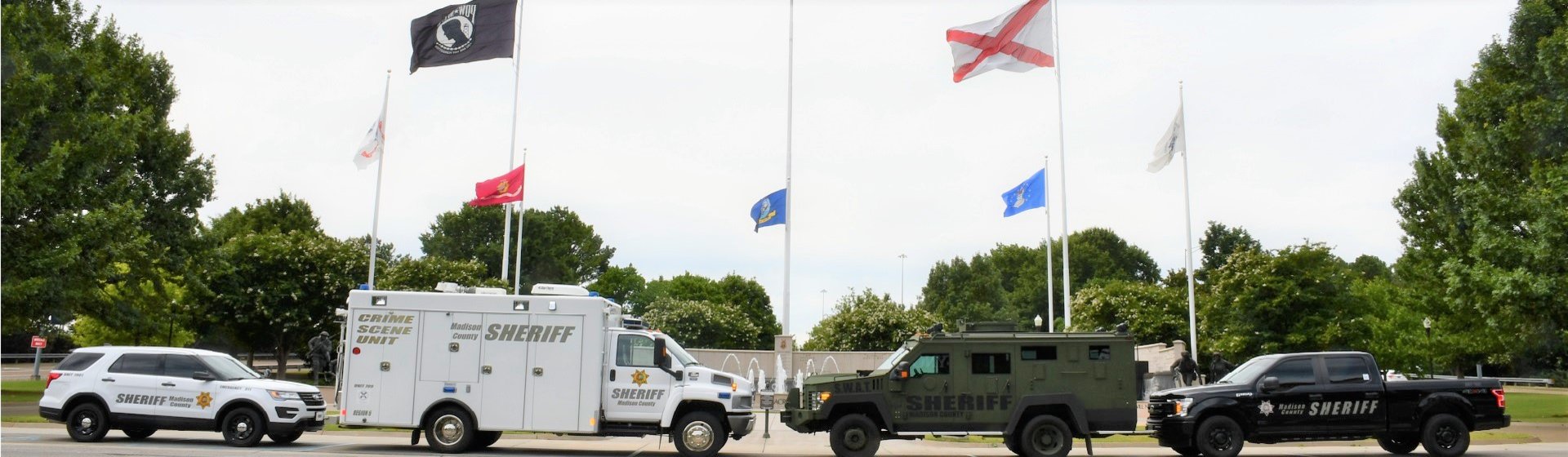 Four Sheriff’s Office vehicles parked in front of Memorial Fountain with flags raised behind the vehicles.